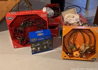 Photo showing boxed 28-inch holiday wreath, pumpkin wreath, plastic tub with ornaments, and boxed LED candle lanterns