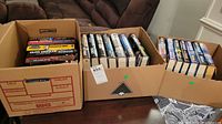 Three cardboard boxes filled with hardcover Clive Cussler books arranged upright and stacked.