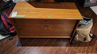 Wooden chest closed, showing smooth wood surface and carved shell-shaped decoration on front panel.