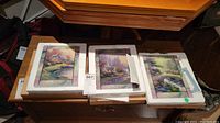 Set of three decorative tiles with framed scenic artwork and certificates of authenticity displayed on wooden surface.