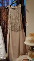 Full view of the champagne colored dress with beaded bodice hanging on a hanger