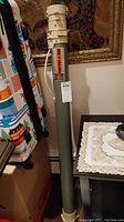 Full length view of olive green cylindrical fishing rod protective case with off-white plastic locking top and strap.