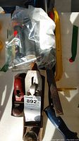View of two metal hand planes, one Stanley branded, red rivet tool, metal file with blue handle, and grease gun tool in plastic bag