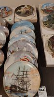 Photo showing seven collector plates arranged in two groups, five with sailing ship themes and two with children and outdoor themes.