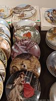 Photo showing multiple collector plates with various scenic and artistic designs stacked and arranged in boxes