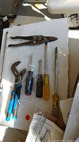 Top-down view of six hand tools including pliers, adjustable wrench, and three screwdrivers on a white surface