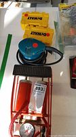 Makita hand sander next to two Dewalt bit cases and red air compressor pump on white surface.