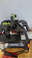 Full view of Rockwell band saw showing black metal table surface, green adjustment knobs, and dust collection bag attached.