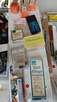 Photo showing various boxed and loose hardware and tools including butt hinge template box, wrap-around box, turntable guide fittings, and a stapler tool.