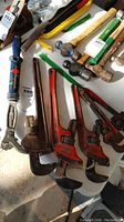 Full view of six heavy duty wrenches on a white surface including three red pipe wrenches, one blue handle adjustable wrench, and two other heavy wrenches with wooden handles and metal heads.