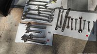 Full view of assorted wrenches laid on white cardboard on pavement, showing set of combination and adjustable wrenches.