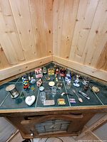 Photo showing all items arranged on a green tiled surface against wood panel walls, overview of collection with varied small items.
