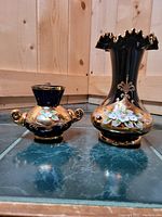 Photo showing both the smaller blue vase and the larger black vase side by side on a tiled floor with wood paneling background.