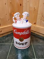 Front view of the Campbell's Kids Soup Can Cookie Jar showing the Campbell's logo and soup label with two kids chefs sitting on the lid, one holding a spoon.