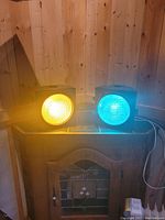 Yellow and greenish-blue vintage street lights on a wooden surface, powered on and illuminated.