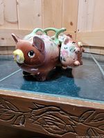 Side view of vintage pig-shaped ceramic condiment set showing larger pig with attached handle and smaller pig hanging from it.