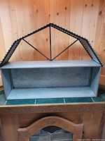 Front view of the metal barn-shaped wall shelf showing its two horizontal shelves and curved corrugated top panel.
