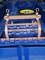 Side angle photo showing vintage pot rack painted in hammered copper finish resting on a blue truck bed with visible hooks and curved supporting steel bands.