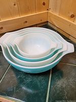 Four nesting bowls, white and blue in color, stacked inside each other showing size progression, set on a tiled countertop in a wood-paneled corner
