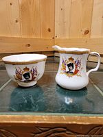 Porcelain creamer and sugar bowl on green surface with wooden background, showing front design.