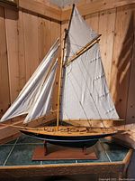 Full view of handcrafted wooden sailing ship model with white sails, rigging, and wooden base.