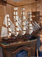 Full front and starboard view of ship model on display base against wooden wall