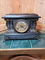 Front view of antique Seth Thomas black mantel clock showcasing dial, columns, and claw feet.