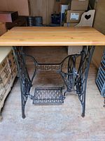 Front view showing Singer sewing machine frame with ornate cast iron detailing and wooden tabletop attached.