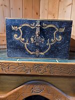Front view of decorative metal treasure chest box with gold scrollwork and lock