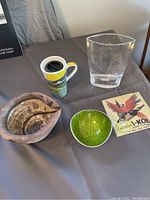 Lot contents on a gray cloth background showing all five art pieces including mug, ceramic bowls, glass vase, and vintage print.