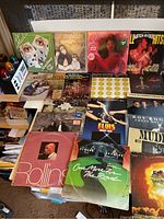 Collection of various classic vinyl LP record covers including The Rolling Stones, The Mamas & The Papas, Elvis Presley, and others shown on a table.