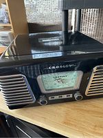 Front view of Crosley radio turntable showing left speaker, tuning dial, volume knob, and Phono/FM/AM switch.