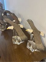 Photo showing two eagle figurines in flight with crystal clear bases, positioned on a wood surface against a wall.