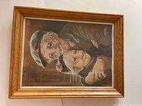 Framed print showing the artwork of an elderly couple, the man wearing a hat and glasses, the woman with a hair accessory, in warm colors.
