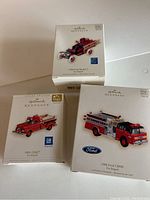 Three boxed Hallmark Keepsake Fire Brigade ornaments showing 1938 Ford Model T, 1961 GMC, and 1988 Ford C8000 models.