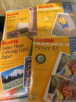 Four sealed Kodak photo paper packages including Premium Picture Paper, Picture Kit, Inkjet Photo Greeting Card Paper, and Matte Photo Paper.