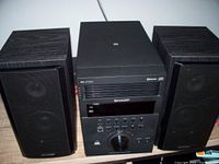 Front view of stereo main unit with CD slot, control buttons, volume knob, and two speakers with black fabric grills and wood finish sides.