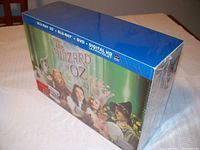 Sealed unopened box with front cover art showing main characters from The Wizard of Oz in front of a green backdrop, including Dorothy, Tin Man, Cowardly Lion, Glinda, and Scarecrow. Blue top band indicates inclusion of Blu-ray 3D, Blu-ray, DVD, and Digital HD Ultraviolet.