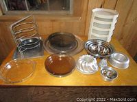 Full set of baking items including pie dishes, bundt pans, mixing bowls, storage units, and rack on wooden table.
