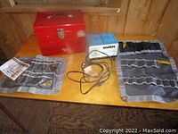 Full lot view on wooden table showing the red metal toolbox, blue Mobie battery charger, and two gray fabric tool storage organizers laid out flat.