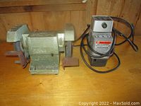 Front view of the bench grinder and drill bit sharpener side by side on a wooden surface