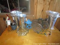 Overview of the lot showing bird feeders, metal pails, rooster figure, plant holders, and string lights on wooden table.