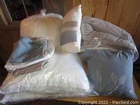 Photo of multiple bedding items including packaged duvet, various pillows and folded bed sheets on a wooden surface