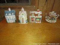 Four ceramic cookie jars resembling different buildings arranged in a row on a wooden surface.