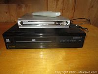 Photo showing the top and front of the DVD player placed on top of the VHS VCR player, view of buttons and disc tray on DVD player and cassette slot on VCR.