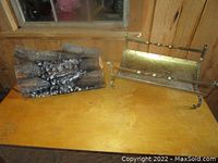 Photo of ceramic fake fireplace with ceramic logs next to brass log holder on wooden surface