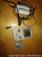 Photo showing the charger, Game Boy console, and one game cartridge laid out on a wooden surface.