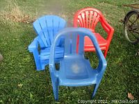 Four kids plastic outdoor chairs in blue and red on grass with some dirt and wear visible