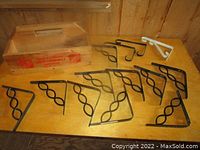 Photo showing 10 black metal shelf brackets with twisted spiral design and 1 white bracket next to a wooden tote with Home Depot logo.