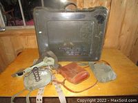 Photo of the thick plastic military case with various pouches and belts displayed on a table in front of it.